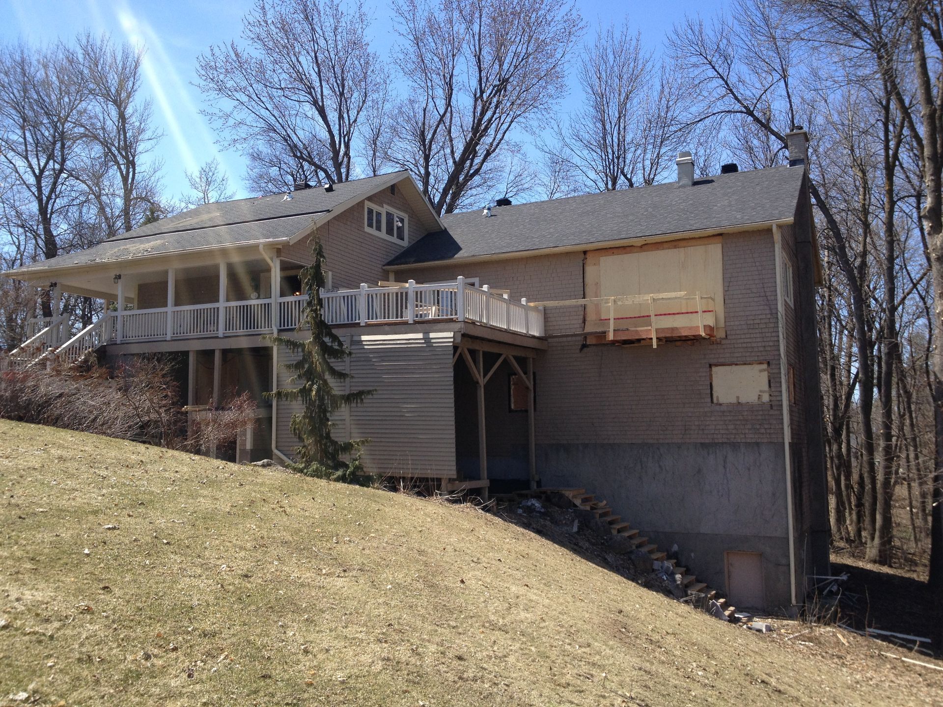 Two-story house with decks, light siding, and unfinished construction on a hillside.