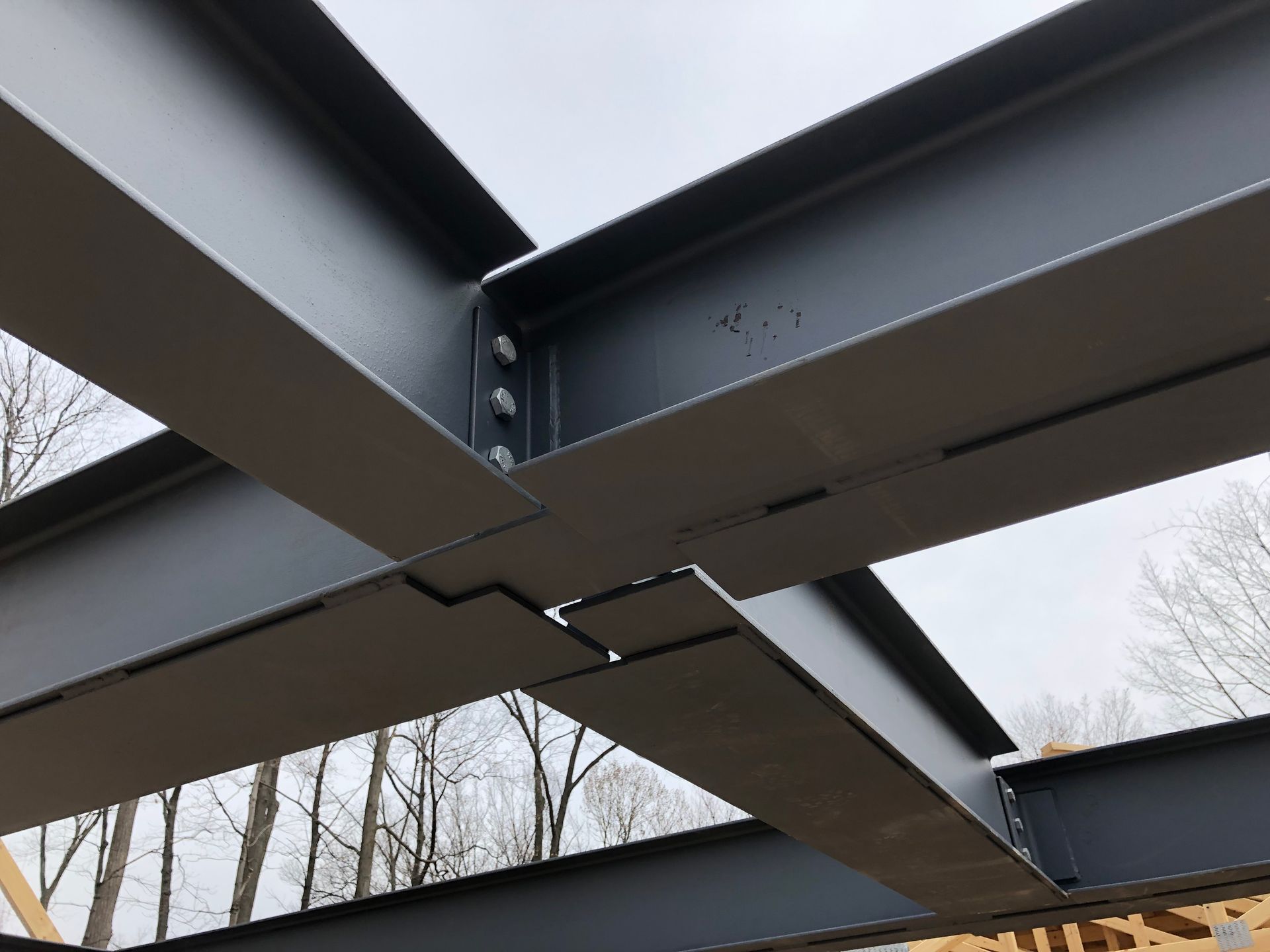Steel beams forming a structural framework, bolted together, set against an overcast sky.