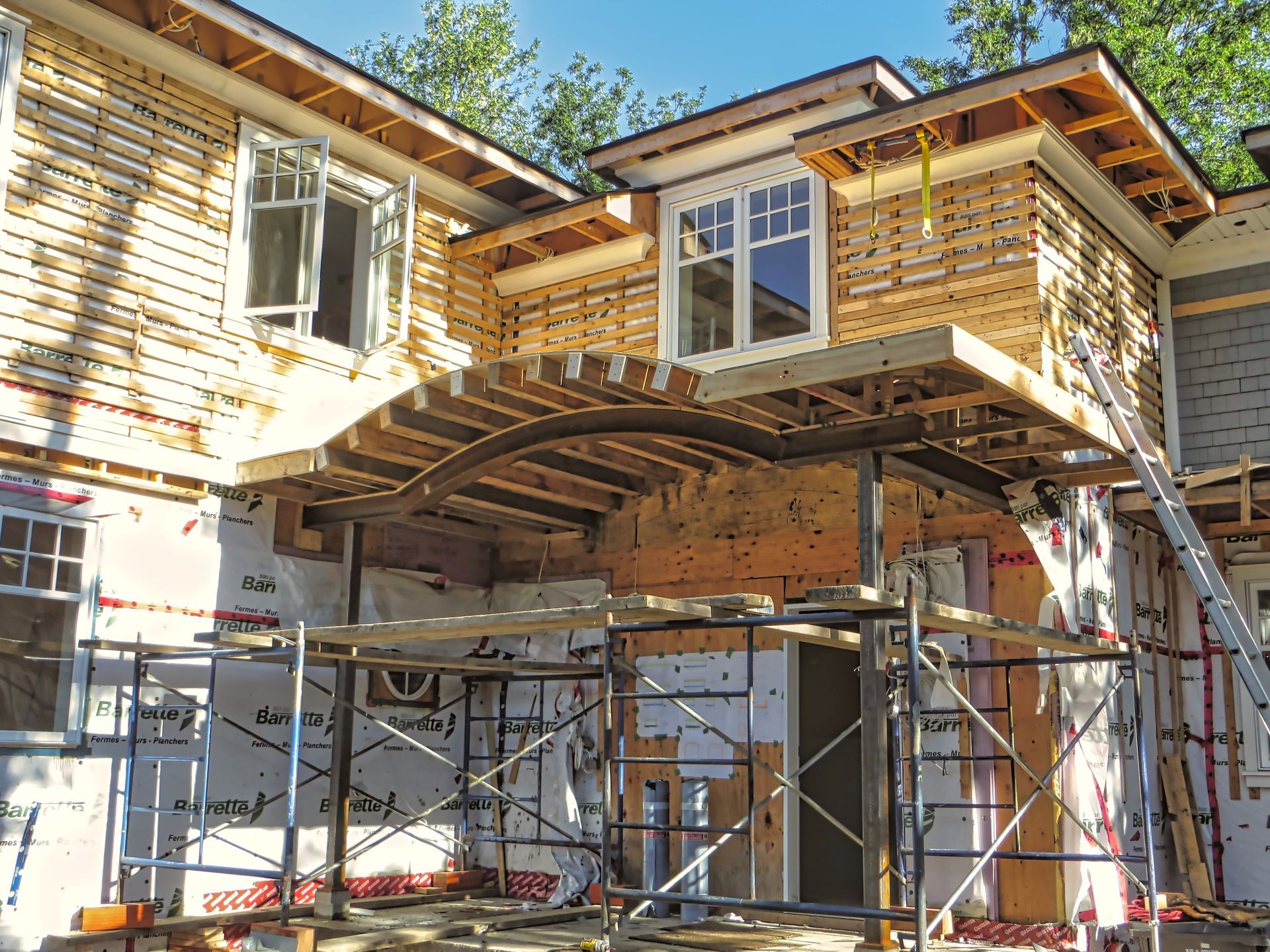 House under construction with scaffolding, exposed framing, and open windows.