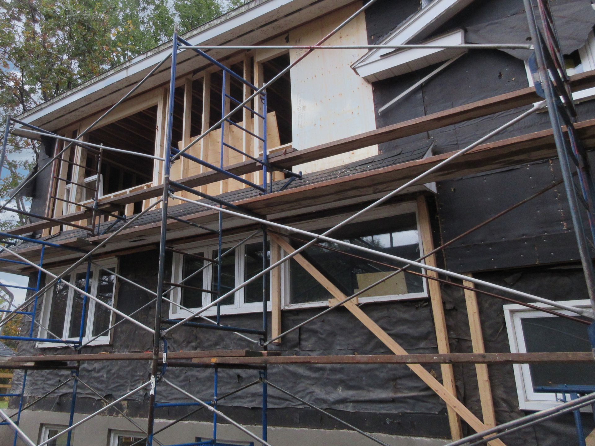 House under construction, with scaffolding. Black sheathing, wooden framing, white windows.