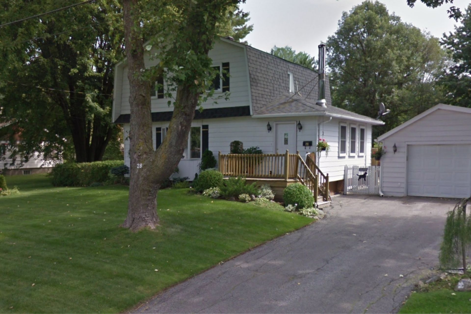 White two-story house with a driveway and attached garage; large tree in front, sunny day.