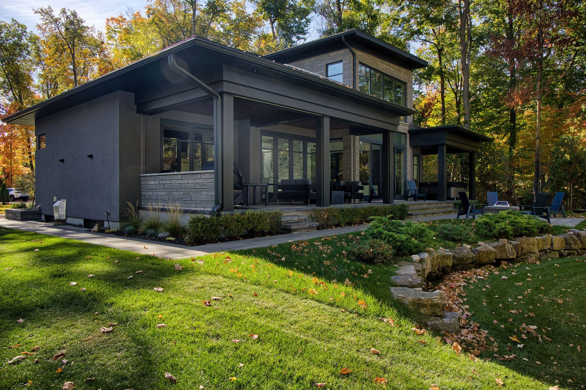 Modern gray house with porch and landscaping in a wooded area with fall foliage.