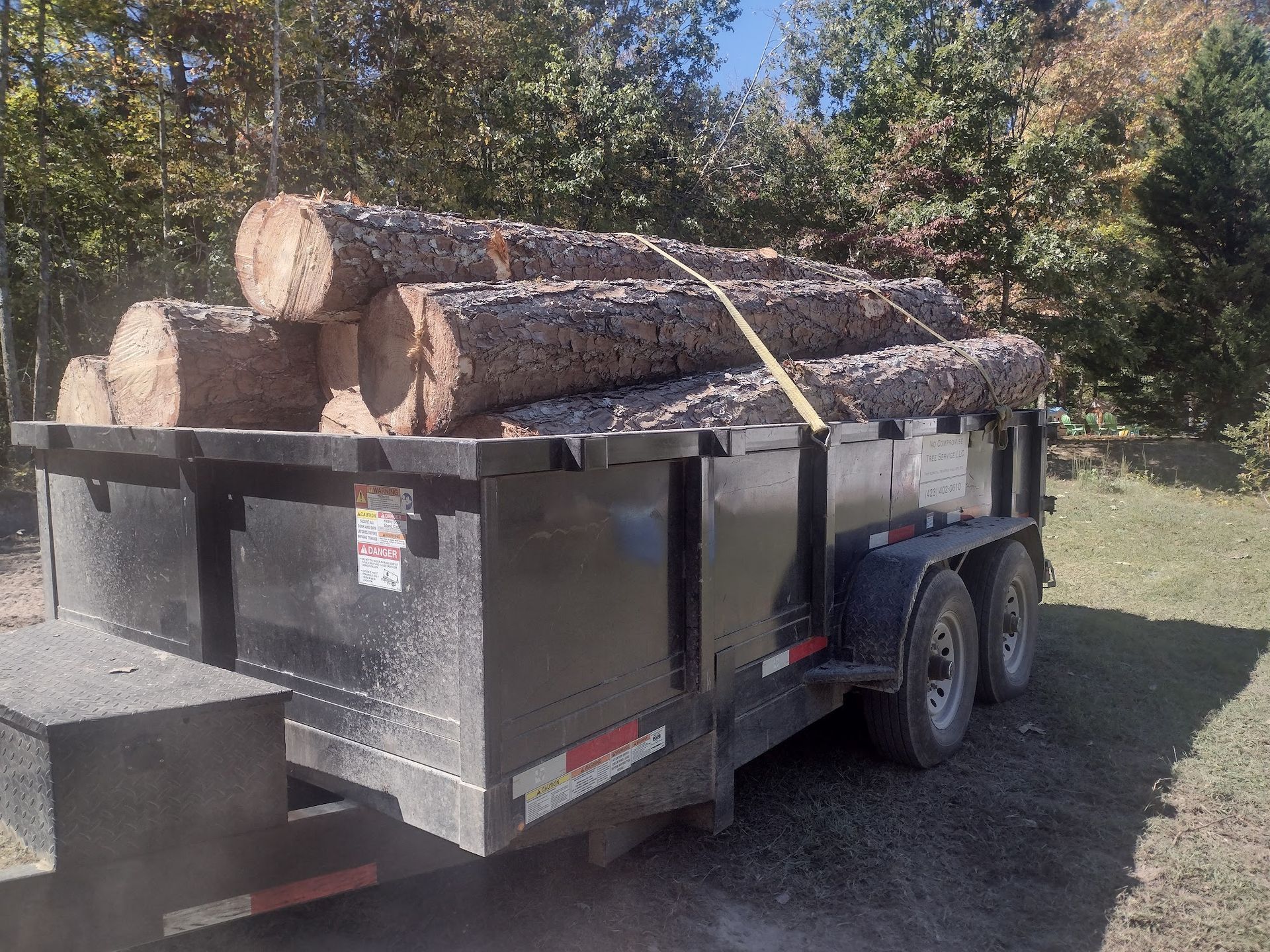 A trailer filled with logs is parked in a field.