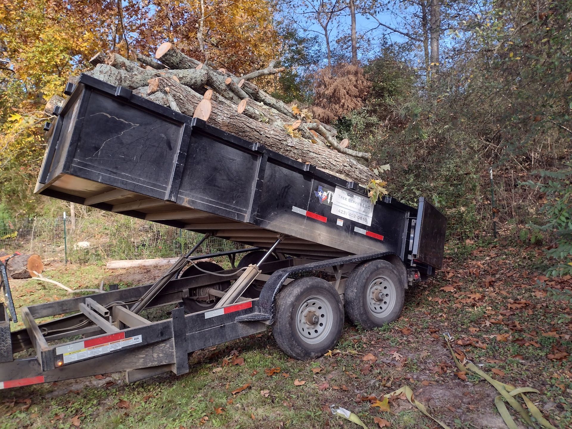 A dumpster is being loaded with logs on a trailer.