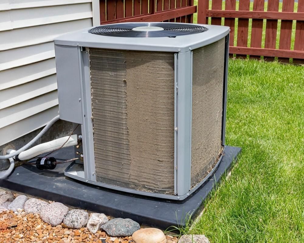 Dirty air conditioner unit on a black base, next to a house and grass.