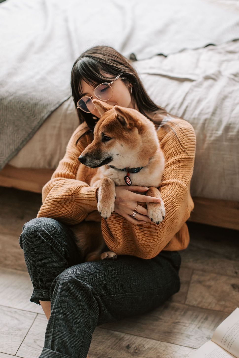 Una persona con un suéter color mostaza está sentada en el suelo, abrazando a un perro Shiba Inu en una acogedora habitación.