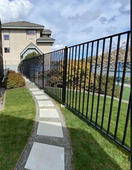 Curved stone walkway beside a black metal fence in a grassy apartment complex courtyard.