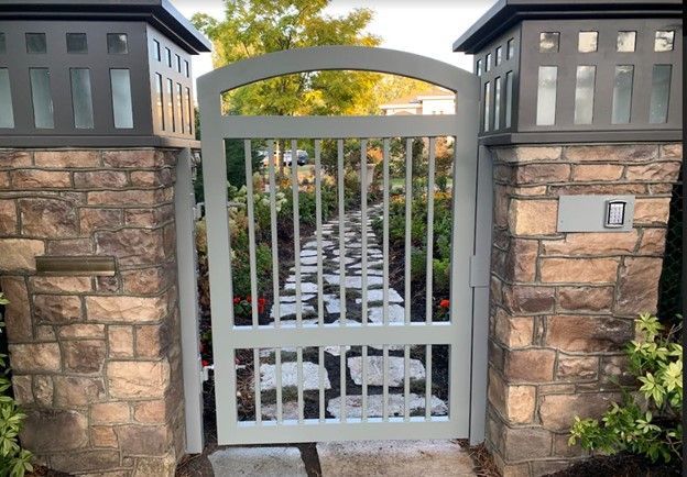 Stone entrance gate with gray metal fence and a pathway leading into a landscaped yard