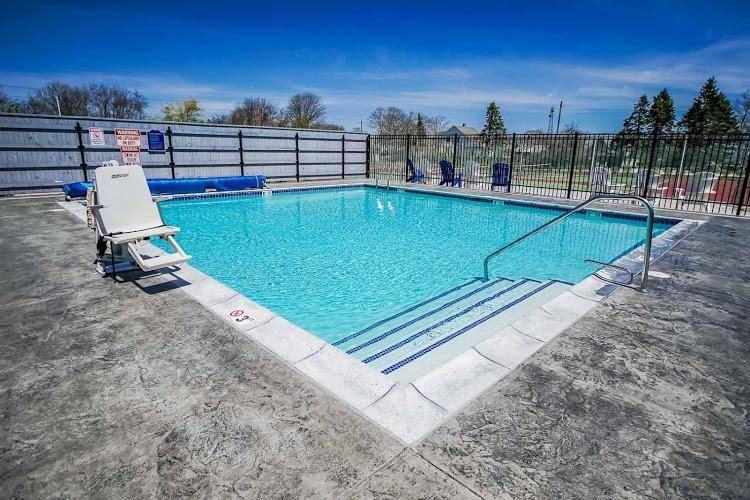 A large swimming pool surrounded by a fence and chairs on a sunny day.