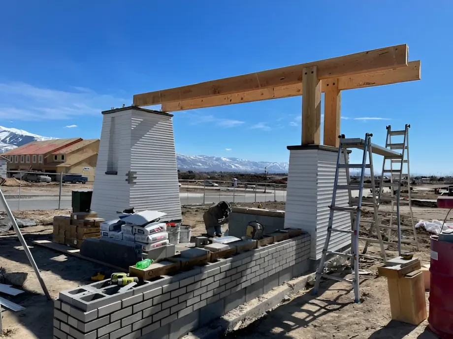 Construction site with brick walls, two white columns, and a large wooden beam supported by scaffolding