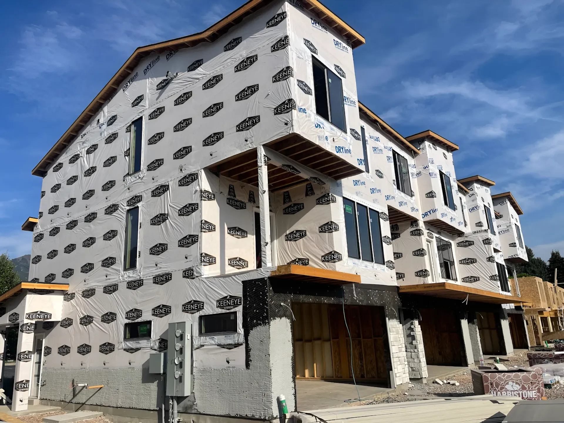 Multi-story apartment building under construction, wrapped in white housewrap with exposed framing and scaffolding.