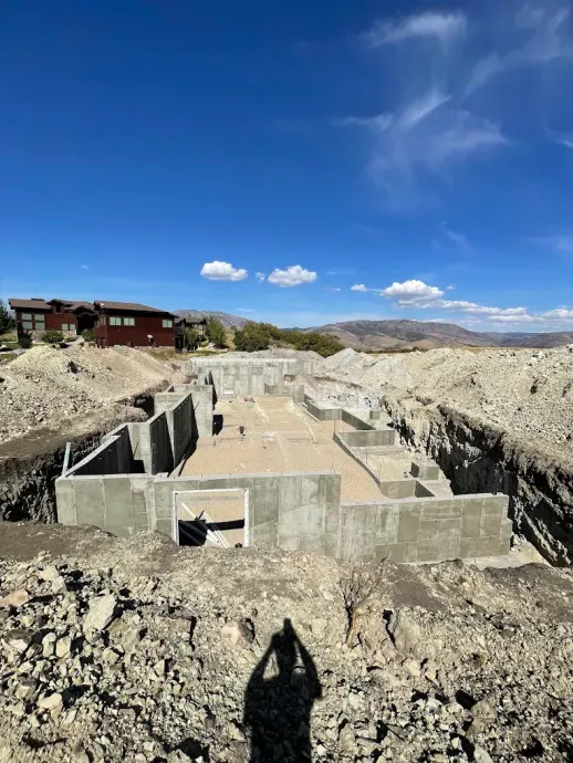 Concrete foundation site in a rocky desert landscape under a bright blue sky with a few clouds