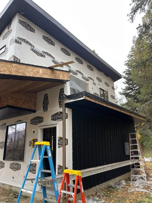 House exterior under construction with black siding, ladders, and a blue step stool outside.