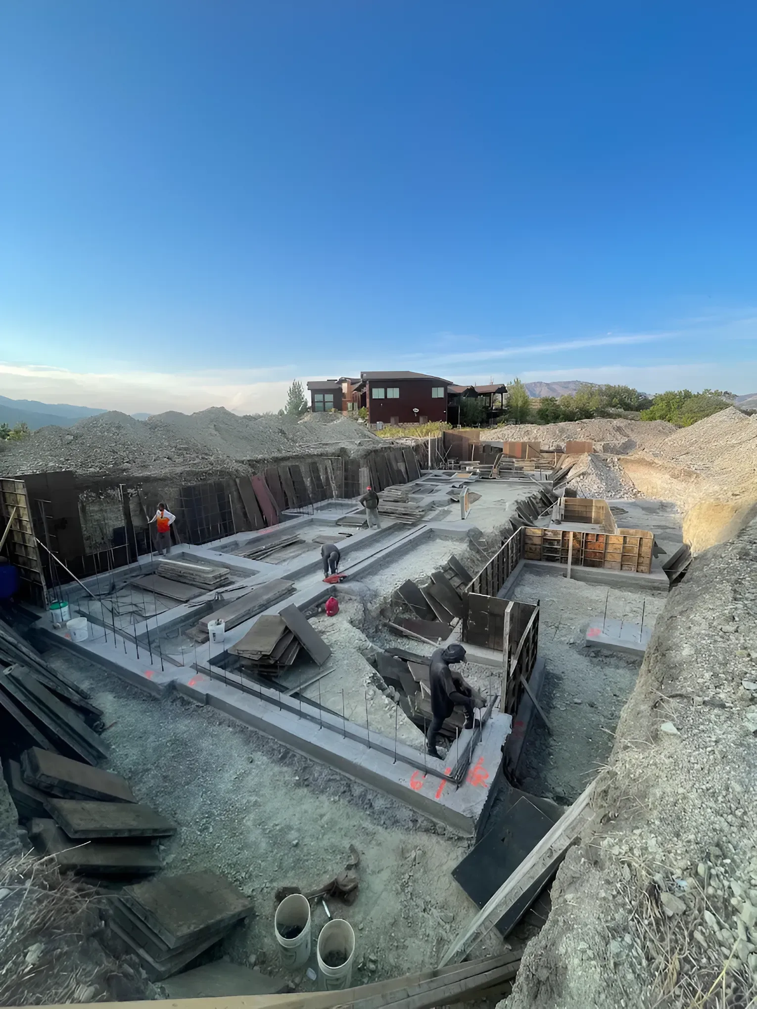 Construction site with rebar foundation, workers, and concrete forms under a blue sky