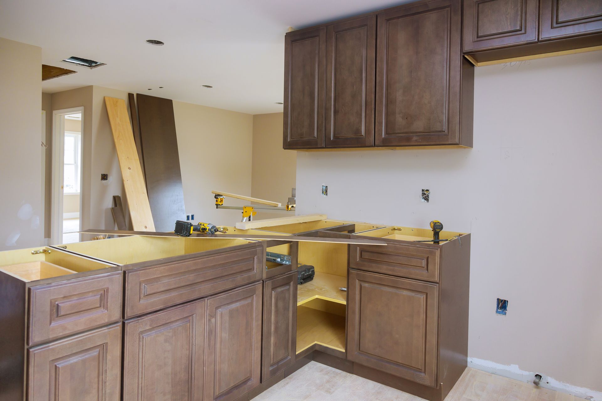 Partially renovated kitchen with unfinished cabinets, yellow countertop, and exposed walls