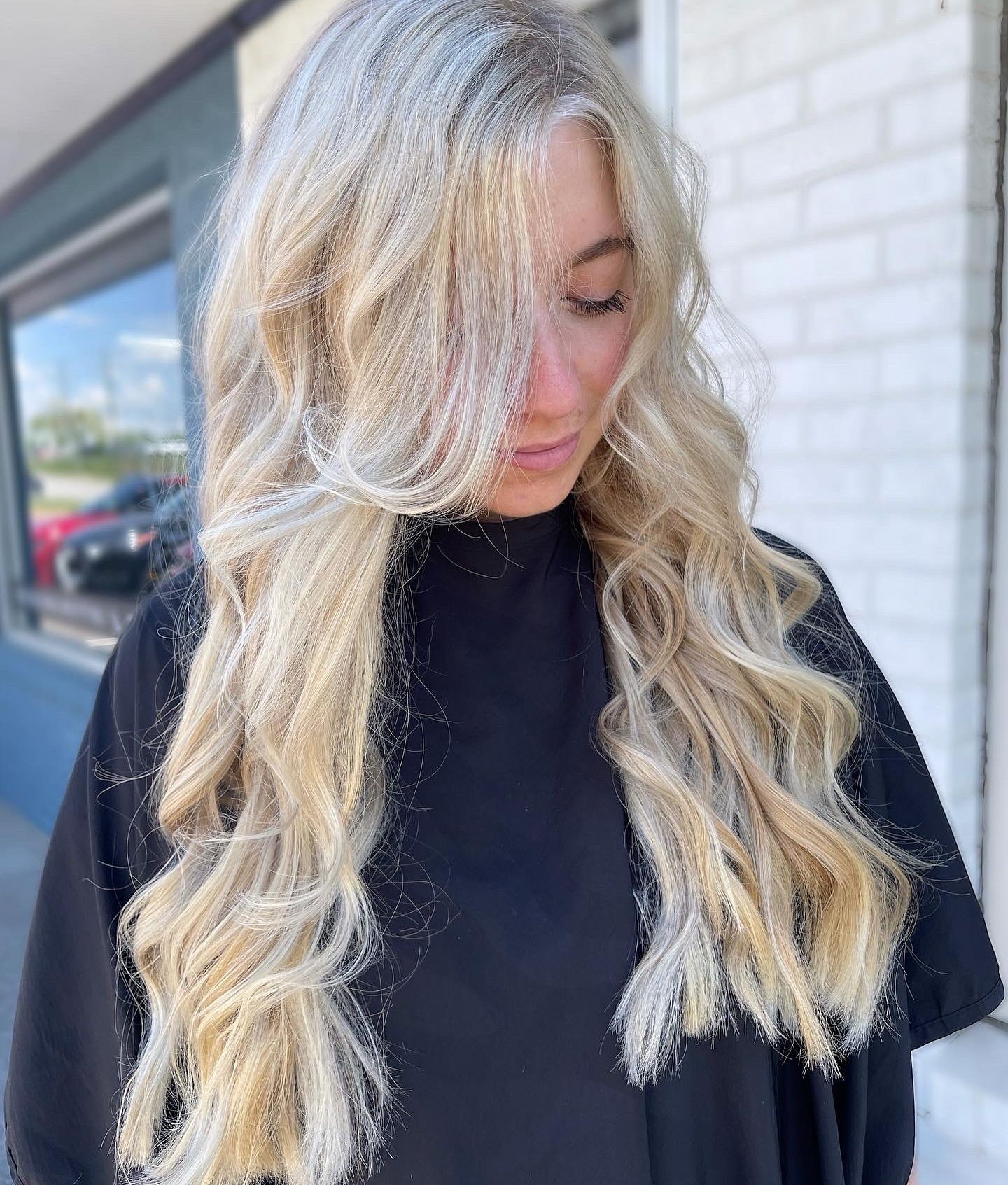 Woman with long blonde wavy hair, wearing a black top, outdoors.