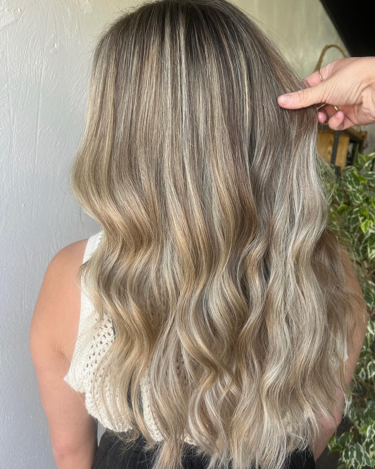 Woman with long, crimped blonde hair, hand touching the hair.