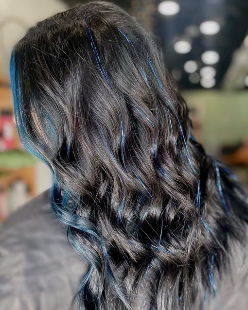 Black wavy hair with streaks of blue tinsel, indoors.