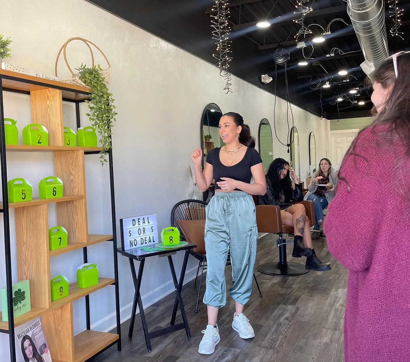 Woman speaking in a boutique, beside shelves of bright green products and a small display table.