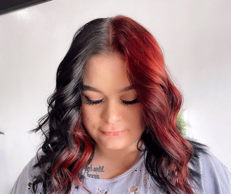 Woman with half black and half red wavy hair, looking down.