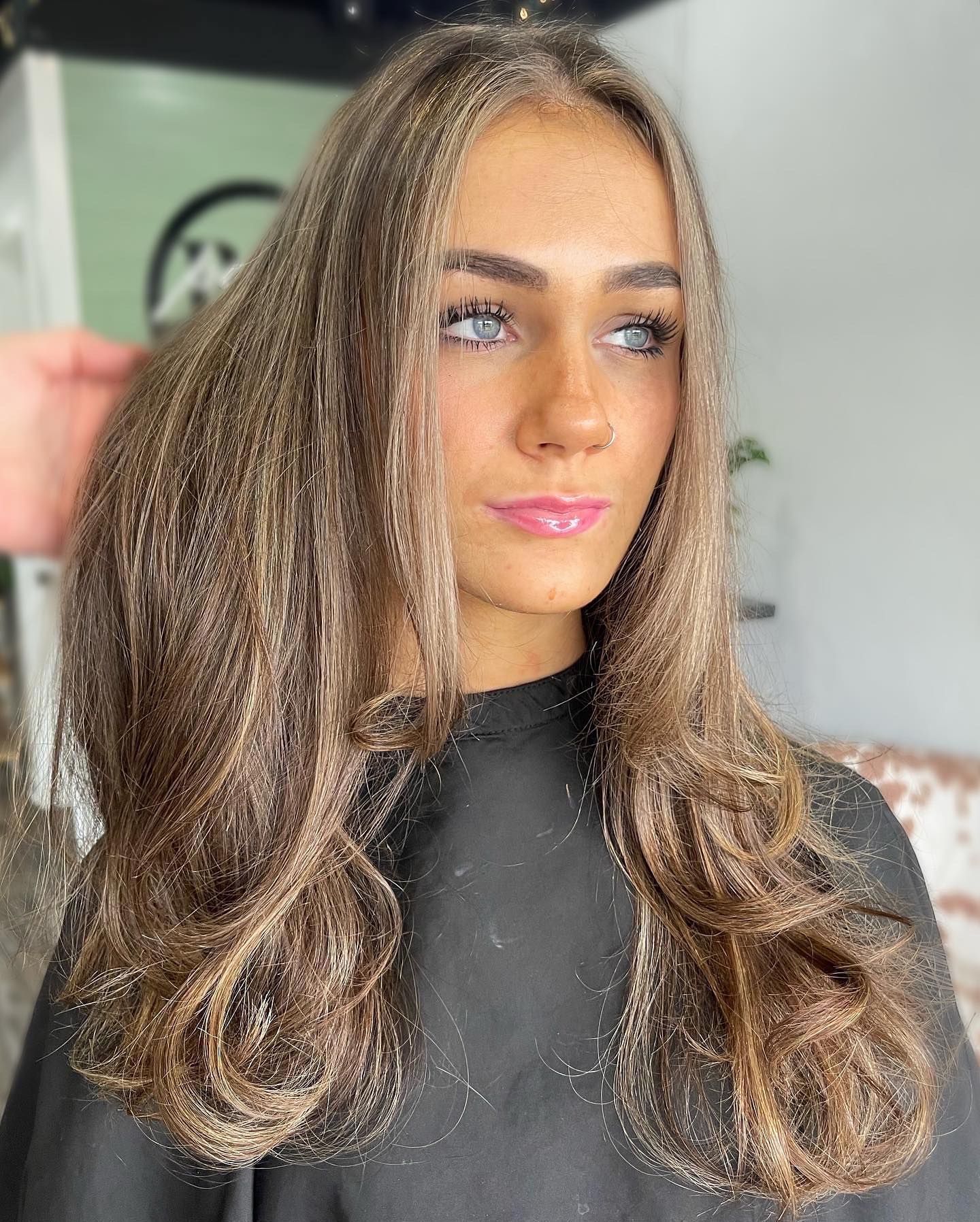 Woman with wavy brown hair, looking to the side, wearing a black salon cape.