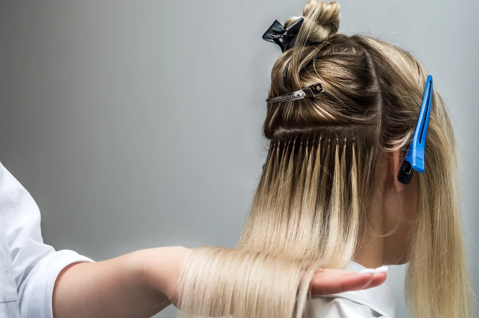 Blonde hair extensions being applied to a person's hair. Hair stylist's hands visible.