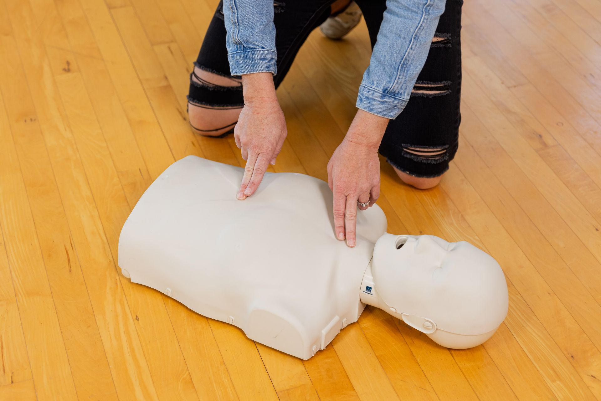 A person is kneeling down next to a mannequin on a wooden floor.