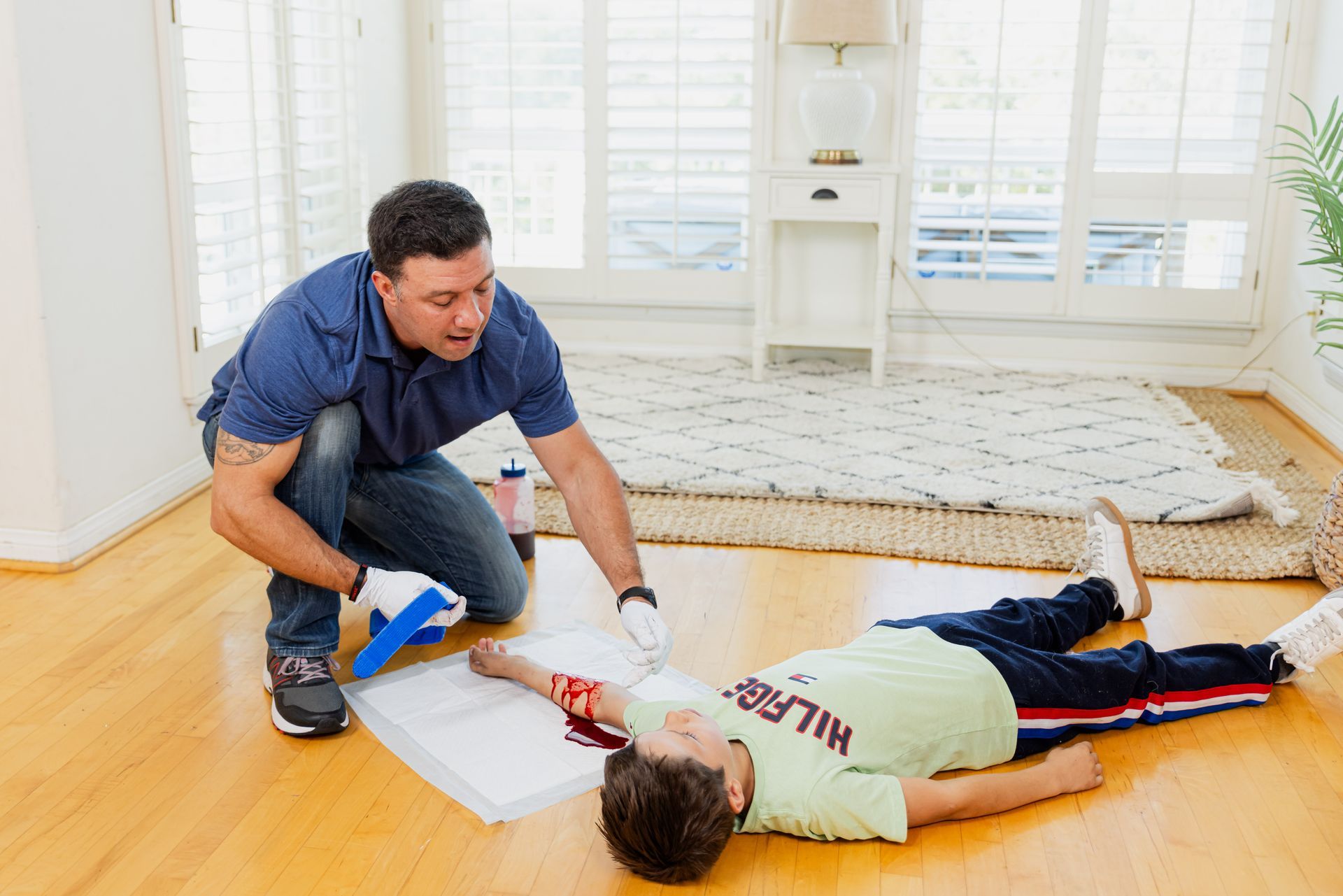 A man is kneeling down next to a boy laying on the floor.