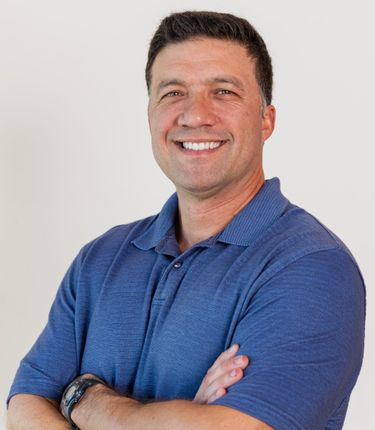 A man in a blue shirt is smiling with his arms crossed.