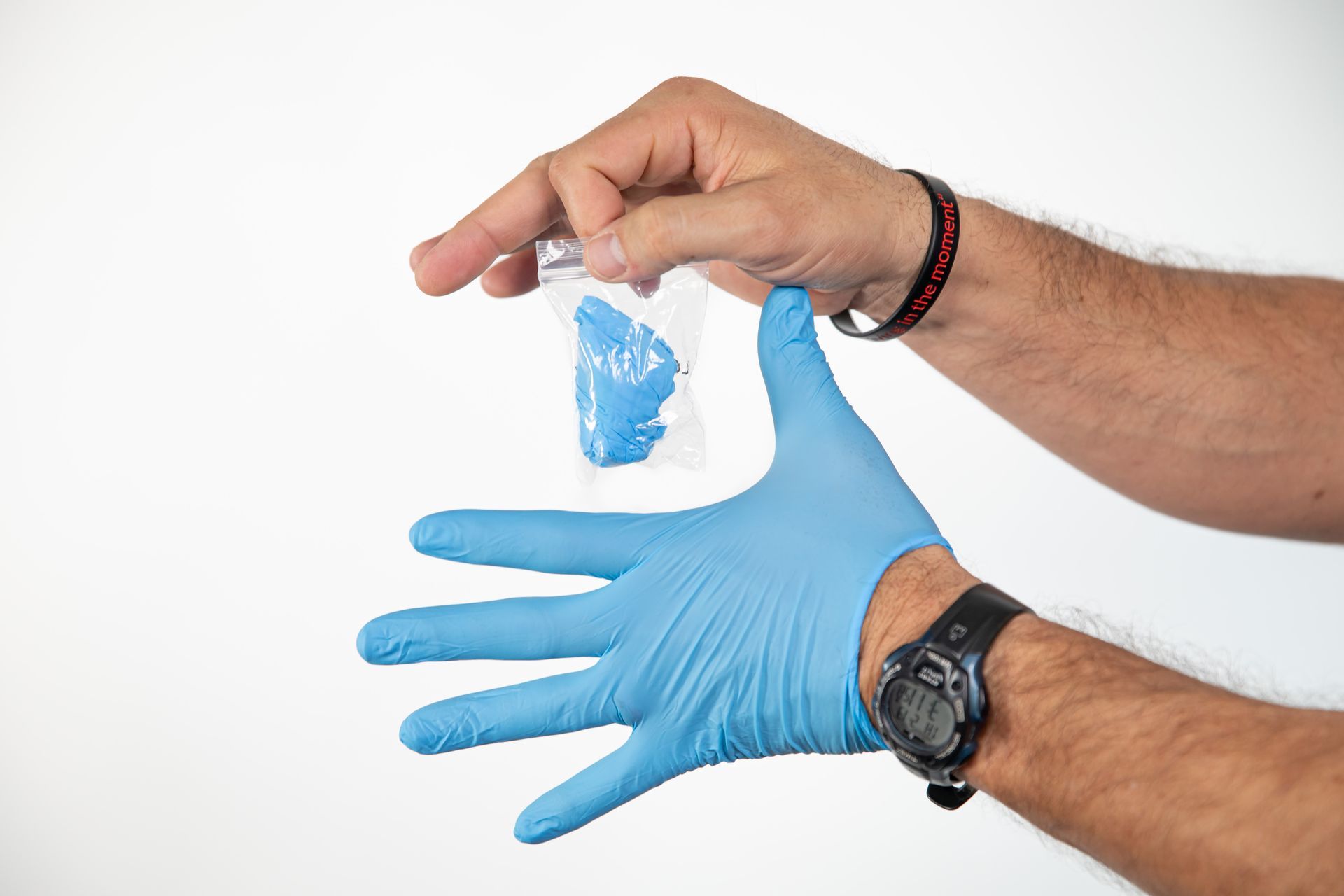 A man wearing blue gloves is holding a small bag of blue substance.
