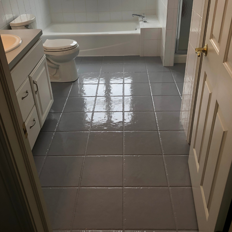 Bathroom with gray tiled floor, white tub, toilet, and vanity. A door frame is on the right.