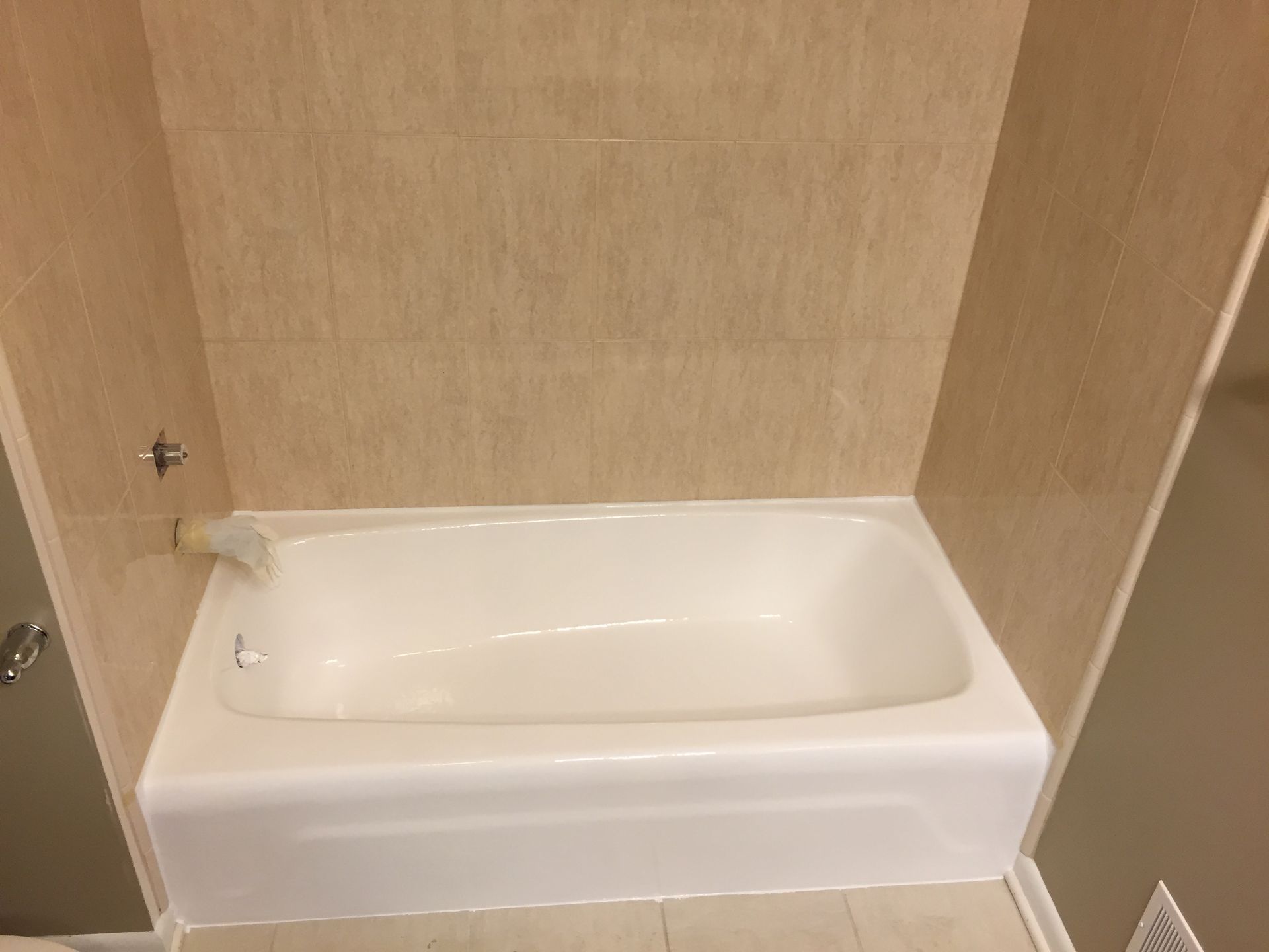 White bathtub with beige tile surround and a faucet, in a bathroom.
