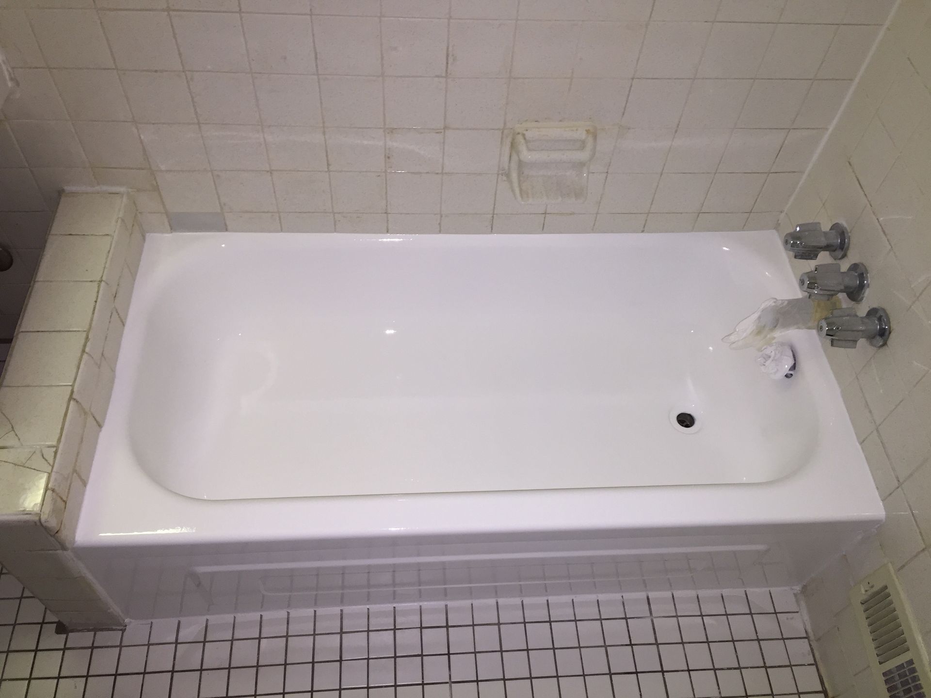 White bathtub with chrome fixtures in a bathroom with white tiled walls and floor.