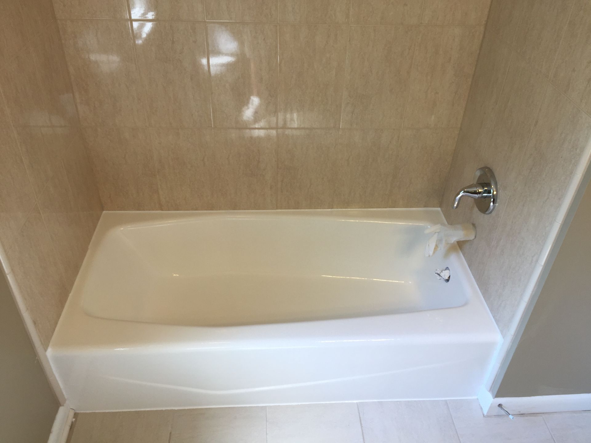 A white bathtub with cream-colored tile walls. A chrome faucet is on the wall.