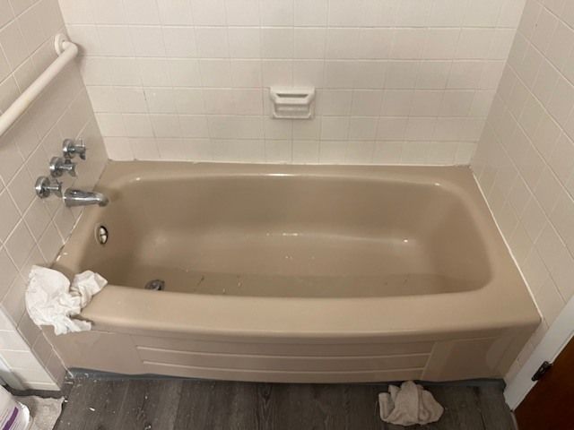 Tan bathtub with chrome fixtures and a white tiled wall. A white hand towel rests on the tub's edge.
