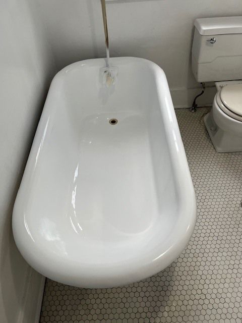 White bathtub with water running from a faucet, next to a toilet on a white tiled floor.