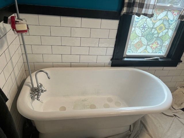 A claw-foot bathtub with a chrome faucet, set against white subway tile walls.
