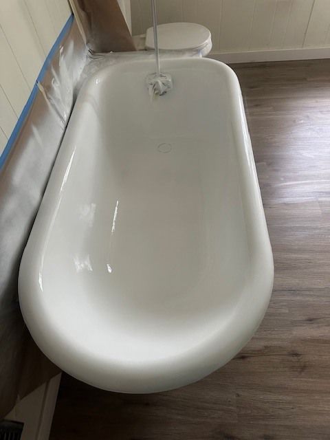White bathtub with rounded sides, partially filled with water, in a room with wood-look flooring.