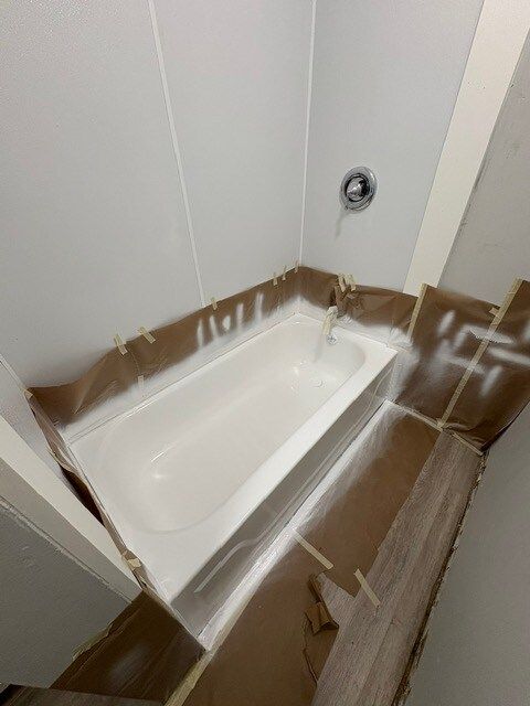 White bathtub in a corner of a bathroom, covered with brown paper and white spray paint.