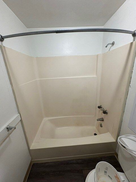 A small, beige-colored bathtub in a bathroom. The shower has a curved rod and is surrounded by beige walls.