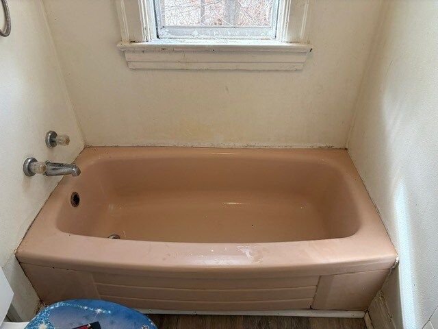 A pink bathtub in a small bathroom, beneath a small window and against cream-colored walls.