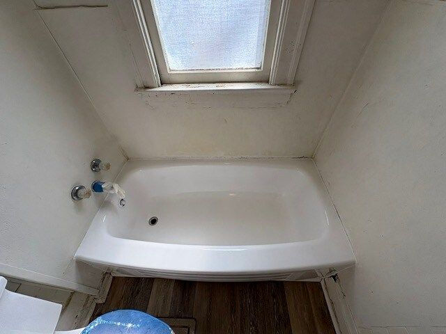 A small, white bathtub in a bathroom with a skylight. The walls are white and the floor is a wood pattern.