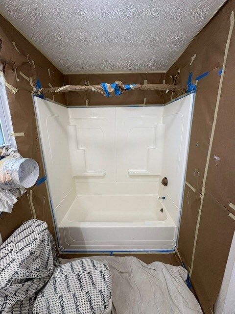 A bathroom with a white shower stall, walls covered in brown paper and tape, ready for renovation.