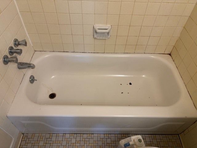 Bathtub with tile surround. A white tub with chrome fixtures and soap dish is set against beige and white tiles.