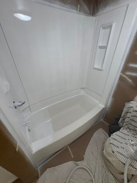 White bathtub and shower surround, freshly painted, inside a bathroom, with masked walls.