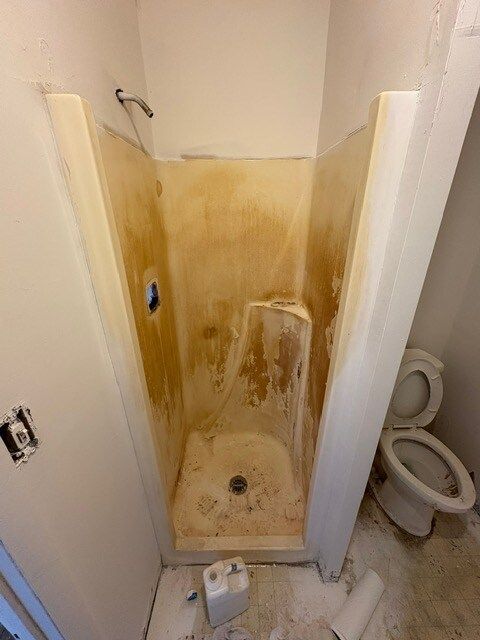A dirty, tan-colored shower stall needing cleaning. A toilet is next to it, and the room is under construction.