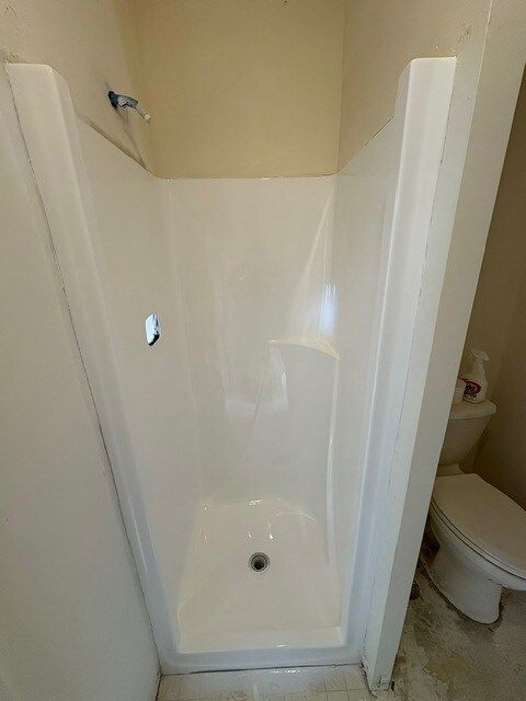 White, stand-up shower stall with a built-in seat. A toilet is visible to the right.