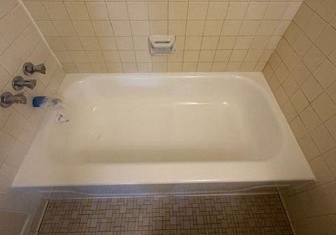 An empty white bathtub against tiled walls and a mosaic-tiled floor.  A soap dish is mounted on the wall above the tub.