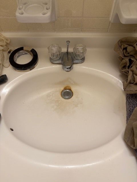 White bathroom sink with water stains, a chrome faucet with clear handles, and a partially visible soap dish above.