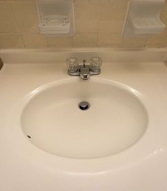White bathroom sink with a chrome faucet, mounted in a white countertop, with soap dishes on the wall above.